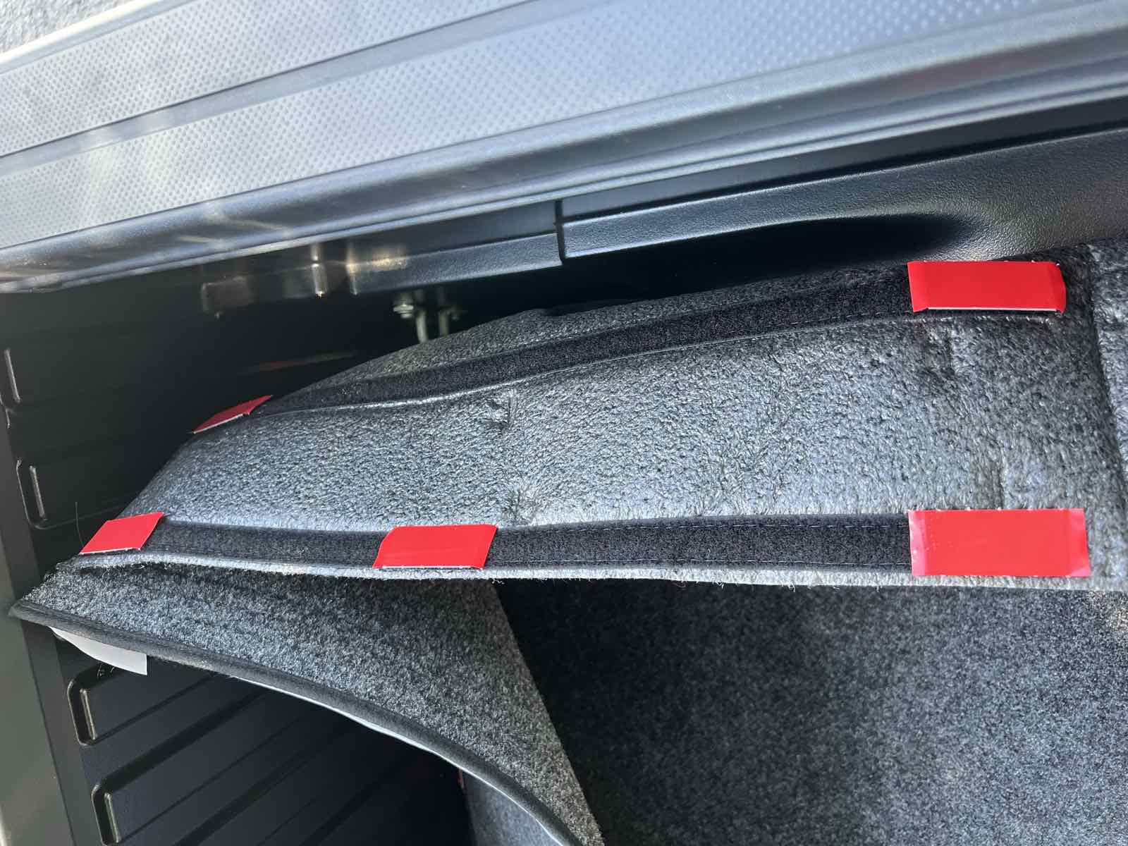 The side wall panel of a bed liner folded back inside a Tacoma bed, showing red adhesive backing tabs along the velcro strips before they are pressed down.