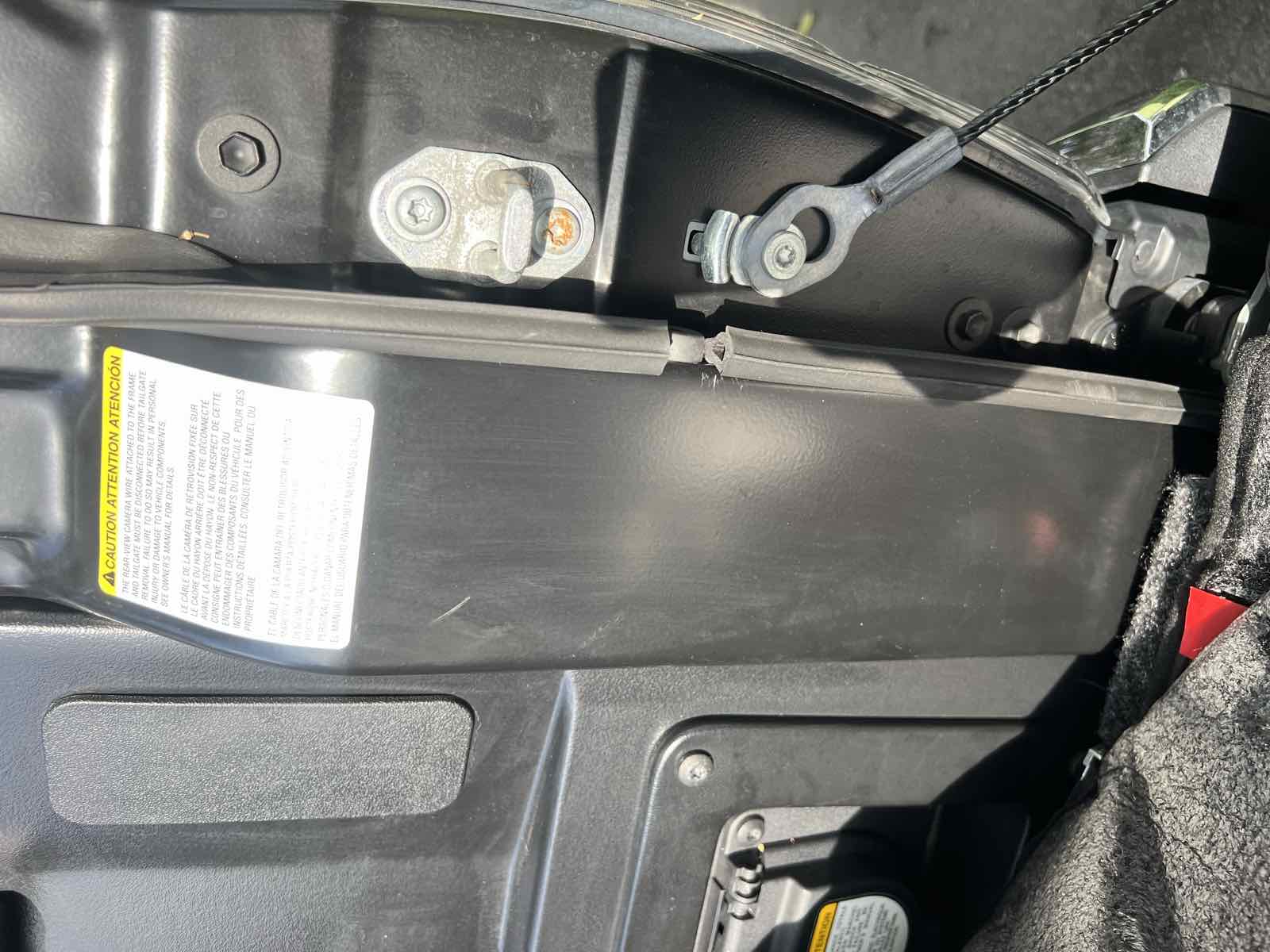 The rear corner of a Toyota Tacoma bed showing the yellow Attention caution sticker, the factory tie-down plate, and the tailgate support cable anchor.
