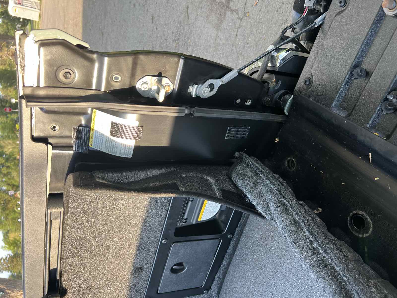The rear corner of a Tacoma bed seen from outside with the tailgate down, showing the molded bed liner edge lifted away from the bed sidewall.