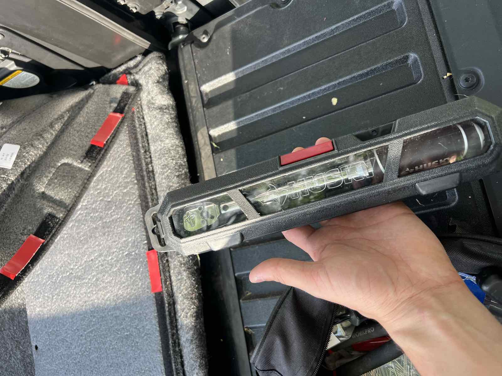 A hand holding a Husky torque wrench still sealed in its retail clamshell packaging, above a truck bed with a bed liner taped in place.