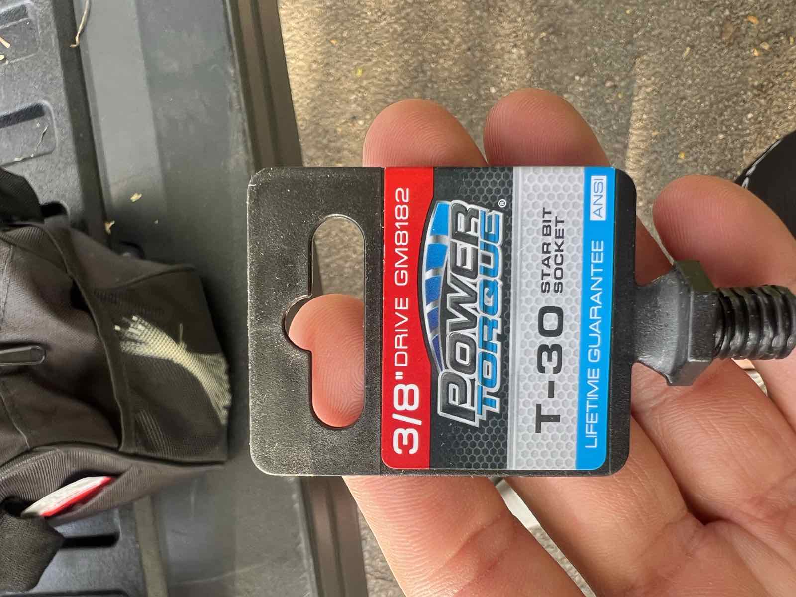 A hand holding a Power Torque T-30 star bit socket in its retail packaging, held over a truck bed.